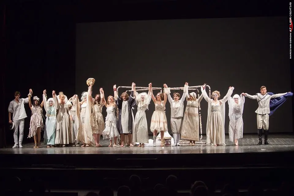 attori in scena su di un palco vestiti in bianco sollevano le mani in via di saluto
